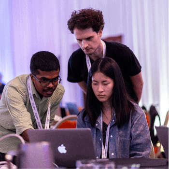 Three hackathon participants collaborating and brainstorming solutions while looking at a laptop.